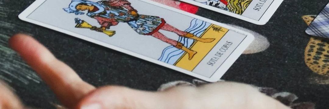 Mão de uma taróloga sobre cartas de tarot abertas num tecido escuro