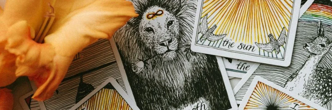 Cartas de tarot ilustradas espalhadas sobre a mesa, ao lado de flores de gladíolo laranja
